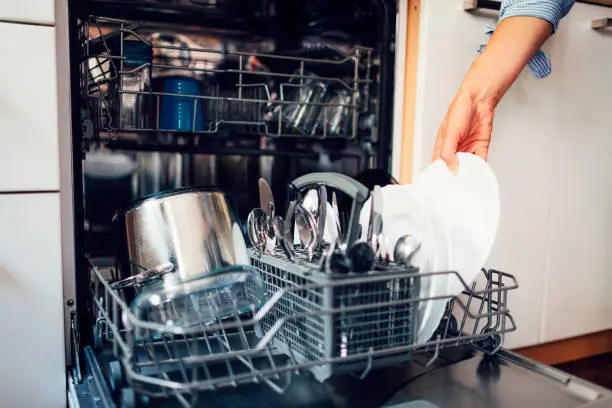 Mid adult woman washing dishes in the kitchen. Cleaning plates after washing with kithen rag