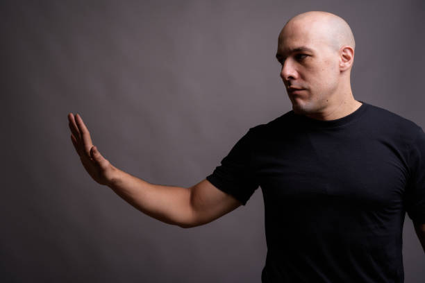 scatto in studio di un uomo calvo muscoloso che indossa una camicia nera su sfondo grigio - hair loss human age side view black and white foto e immagini stock