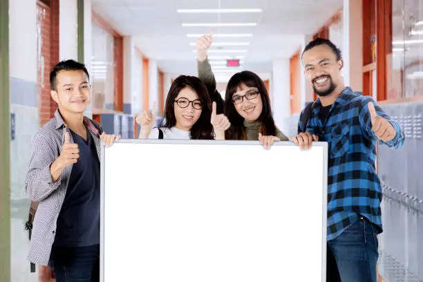 College students showing ok sign while holding empty billboard in the school corridor