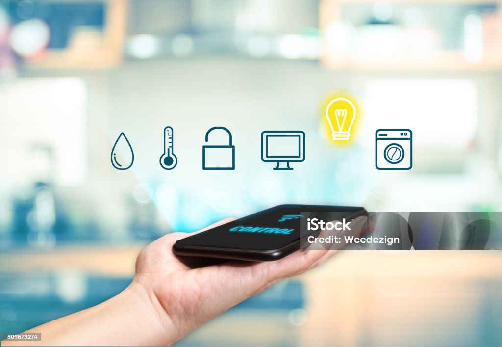 Hand holding mobile with Smart home control icon feature with blur kitchen background,Digital Lifestyle concept Home Automation Stock Photo