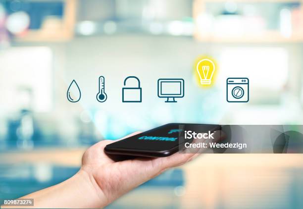 Hand Holding Mobile With Smart Home Control Icon Feature With Blur Kitchen Background Digital Lifestyle Concept Stock Photo - Download Image Now
