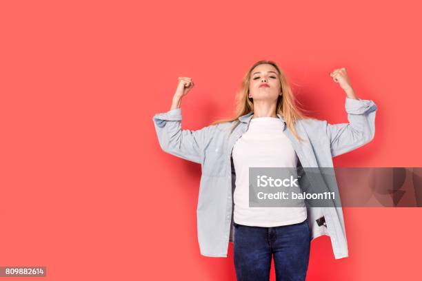 Young Blonde Girl Shows Her Strength On Red Background Stock Photo - Download Image Now
