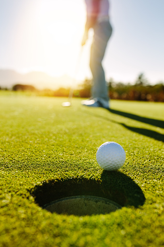 Golf ball at the edge of hole with player in background. Professional golfer putting ball into the hole on a sunny day.