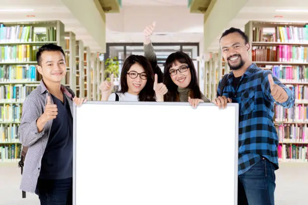Multi ethnic of young people showing ok sign and empty board while standing in the library