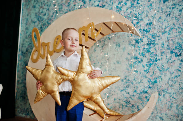 istock Cute small handsome boy posing on artificial moon decoration while holding star-shaped cushion. 809925016
