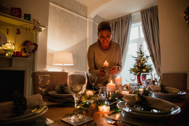 Setting The Table For Christmas Dinner Happy mother is setting the table for Christmas dinner with her family.  She is lighting candles. low lighting stock pictures, royalty-free photos & images