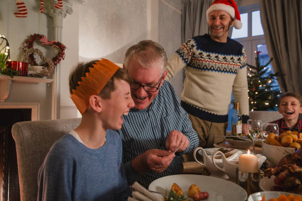 Telling Christmas Cracker Jokes Little boy is laughing as his grandfather tells him a joke from a christmas cracker at the dinner table. funny thanksgiving stock pictures, royalty-free photos & images