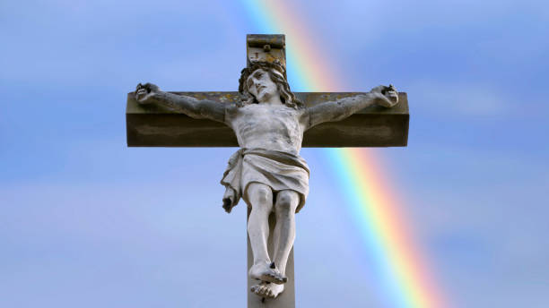stone cross with Jesus and blue sky with rainbow