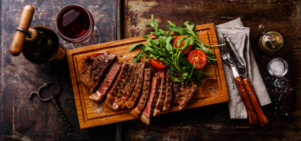 steak with arugula salad and Red wine Sliced grilled beef barbecue Striploin steak with arugula salad and Red wine on dark background steak salad stock pictures, royalty-free photos & images