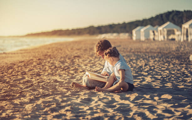 istock Children reading a book on beach at sunset 809986352