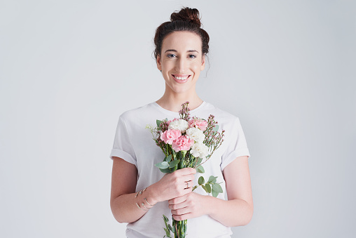 Studio shot of a beautiful young woman holding a bouquet of flowers against a grey background