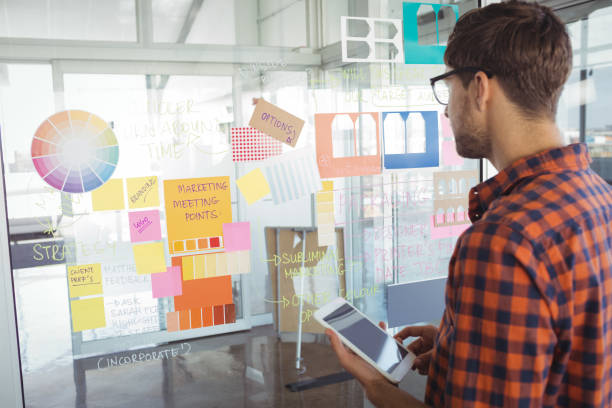 istock Businessman holding mobile phone while looking at adhesive notes in office 810067436