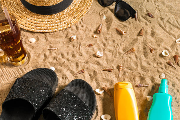 istock Summer beachwear, flip flops, hat, cold drink in a glass and seashells on sand beach 810081724