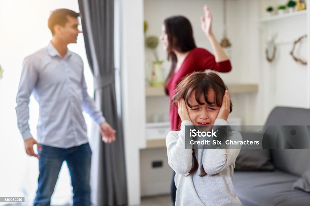 Crying girl with his fighting parents in the background, Sad gril while parents quarreling in the living room Family Stock Photo