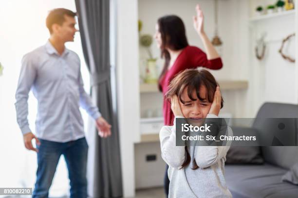 Crying Girl With His Fighting Parents In The Background Sad Gril While Parents Quarreling In The Living Room Stock Photo - Download Image Now