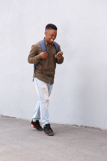 istock Full body black male student walking with cellphone and bag 810099748