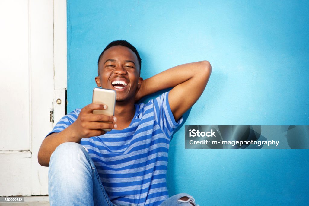 young african man laughing and looking at cellphone Portrait of young african man laughing and looking at cellphone African Ethnicity Stock Photo