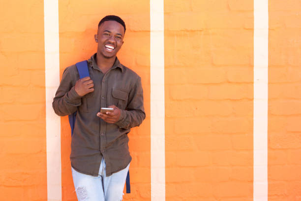 istock happy black guy laughing with cell phone against orange wall 810099822