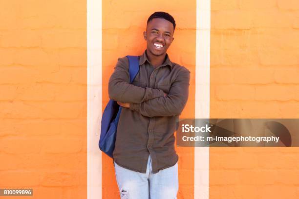 Happy African Male Student Standing Against Orange Wall With Bag Stock Photo - Download Image Now
