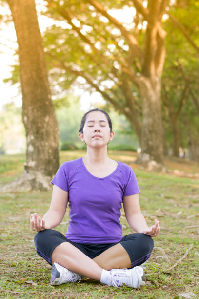 istock Asian woman meditating alone on yard in the park with sun light 810110364