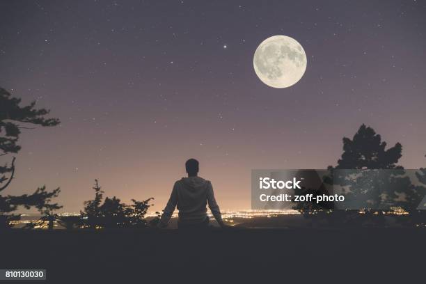 Man Enjoying The View From Hill Above City Full Moon And Stars On The Sky Stock Photo - Download Image Now