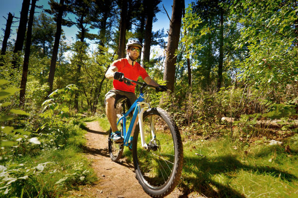 A Caucasian young man mountain biker biking along a wooded mountain trail. Photographed in the midwest USA in horizontal format.