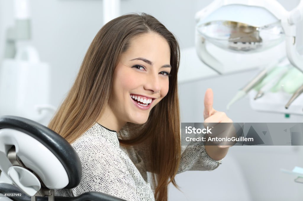 Dentist patient satisfied after treatment Patient with perfect white teeth and smile satisfied after dental treatment in a dentist office with medical equipment in the background Dental Equipment Stock Photo