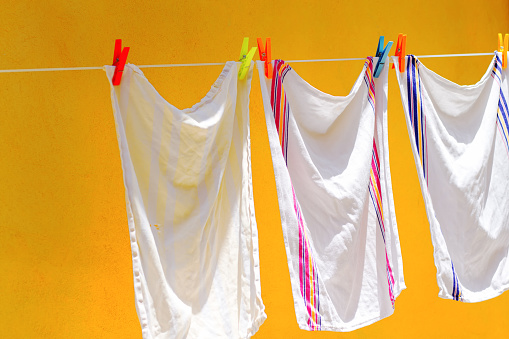 Italy: White dish towels on a laundry line (clipped with colorful clothes pins) against a vibrant yellow wall. The white towel on the left is well used, with a little hole in it. Copy space available.