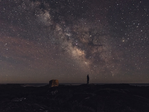A man is silhouetted against the summer Milky Way stretching high overhead.  Long exposure.