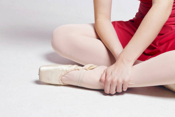 バレリーナは白い床に座って彼女の足に触れます。 - ballet people dancing human foot ストックフォトと画像
