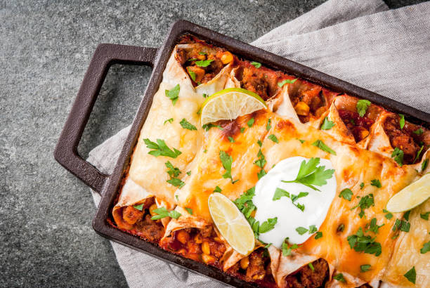 Spicy beef enchiladas Mexican food. Cuisine of South America. Traditional dish of spicy beef enchiladas with corn, beans, tomato. On a baking tray, on a black stone background. Top view copy space enchilada stock pictures, royalty-free photos & images