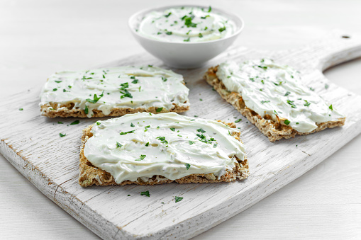 Homemade Crispbread toast with Cream Cheese and parsley on white wooden board background.