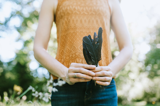 Beauty in style and fashion, as well as natural beauty of nature; a young adult woman models her fashion sense with some feathers she found in a sunlit field.