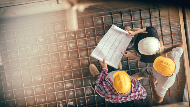 Female architect and two consruction workers on a construction site High angle view of three people with helmets, female architect, foreman and engineer on a construction site, looking down on a blueprint, copy space. drawing activity photos stock pictures, royalty-free photos & images