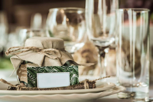 istock Rustic table setting for a wedding celebration in nice cozy restaurant. Wineglasses, plates and food on a table. Guests complement in a rustic jar. Nice card with a space for text 810318014