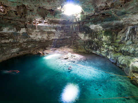 Young, white, caucasian, male man swimming in natural pool, cave, cenote Samula, illuminated by light, sunbeam from above, close to Valladolid, Mexico