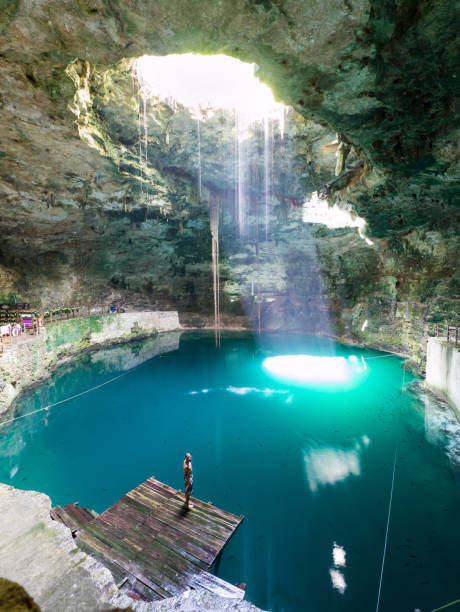 Young man standing in cenote Hubiku in mexico Young, white, caucasian, male man standing on wooden pier in natural pool, cave, cenote Hubiku, illuminated by light, sunbeam from above, close to Valladolid, Mexico cenote stock pictures, royalty-free photos & images