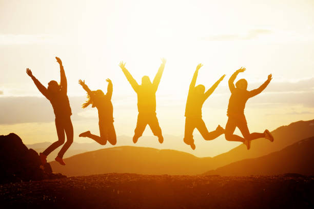 Happy friends jumping sunset mountains Group of five happy friends jumps at sunset time on background mountains group mountain silhouette stock pictures, royalty-free photos & images