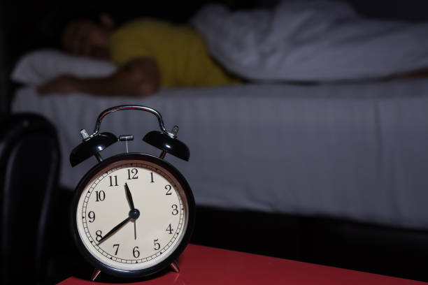 istock Alarm clock at 11:39 pm on bedside table in bed male sleeping in background, man rest in dark room at night 810521084
