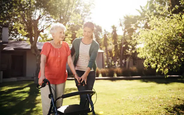Shot of a senior mother using a walker while out for a walk in the garden with her daughter