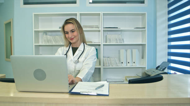 istock Smiling medical nurse working on laptop and making notes at reception desk 810532806