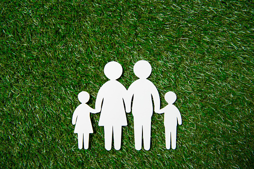 top view of white paper figures of family on grass meadow
