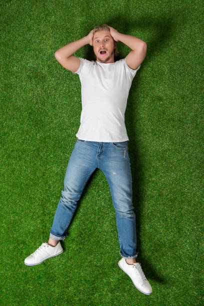 istock young astonished man with hands on head lying on the meadow 810534422