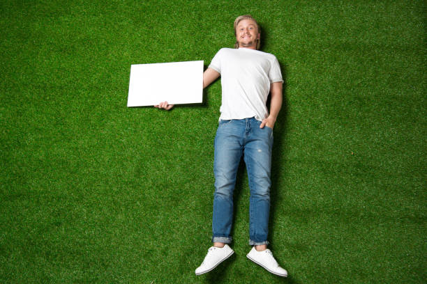 istock above view of young man holding blank placard while lying on meadow 810536040