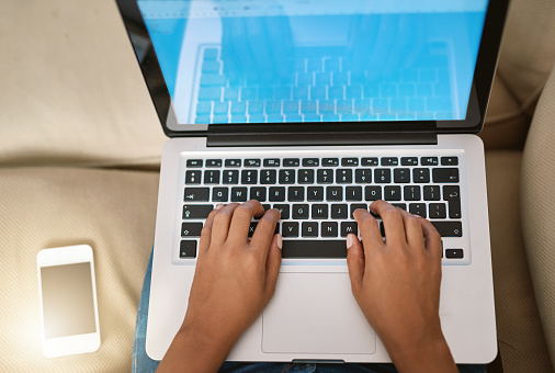 Cropped shot of a woman using her laptop on the sofa at home