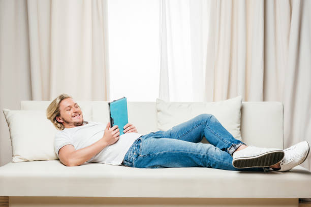 istock smiling man in white t-shirt and jeans using digital tablet while lying on sofa at home 810547844
