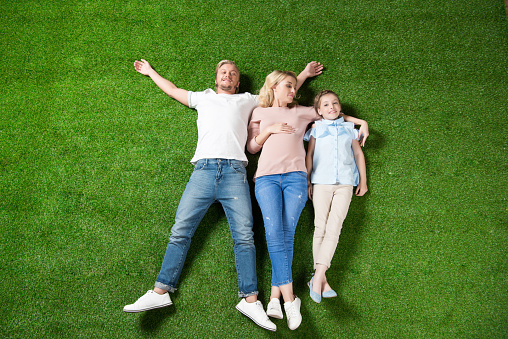 top view of parents and daughter lying together on green grass