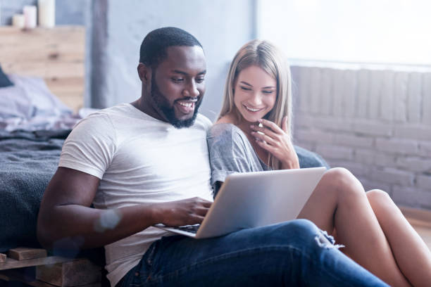 istock Amused international couple using laptop at home 810556504