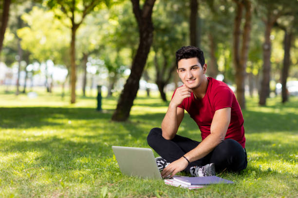 Teenage student working with laptop in park.