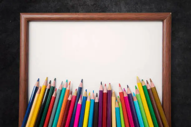 Top view of colored pencils over a blank frame on the blackboard